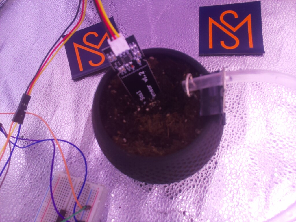 Container filled with soil. Electronic components and irrigation tubing visible. No visible plant growth detected.